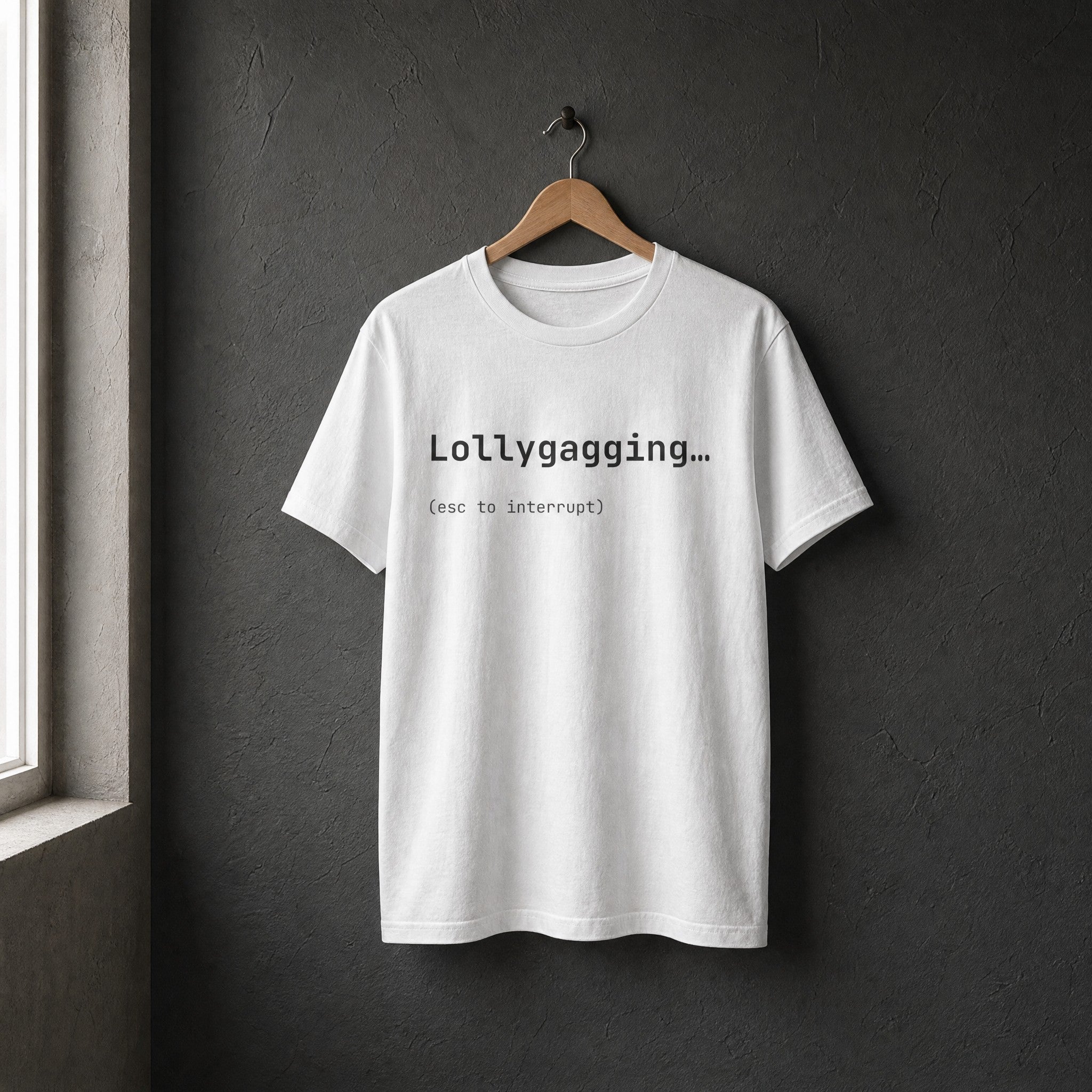 White Lollygagging esc to interrupt t-shirt on a wooden hanger against charcoal wall