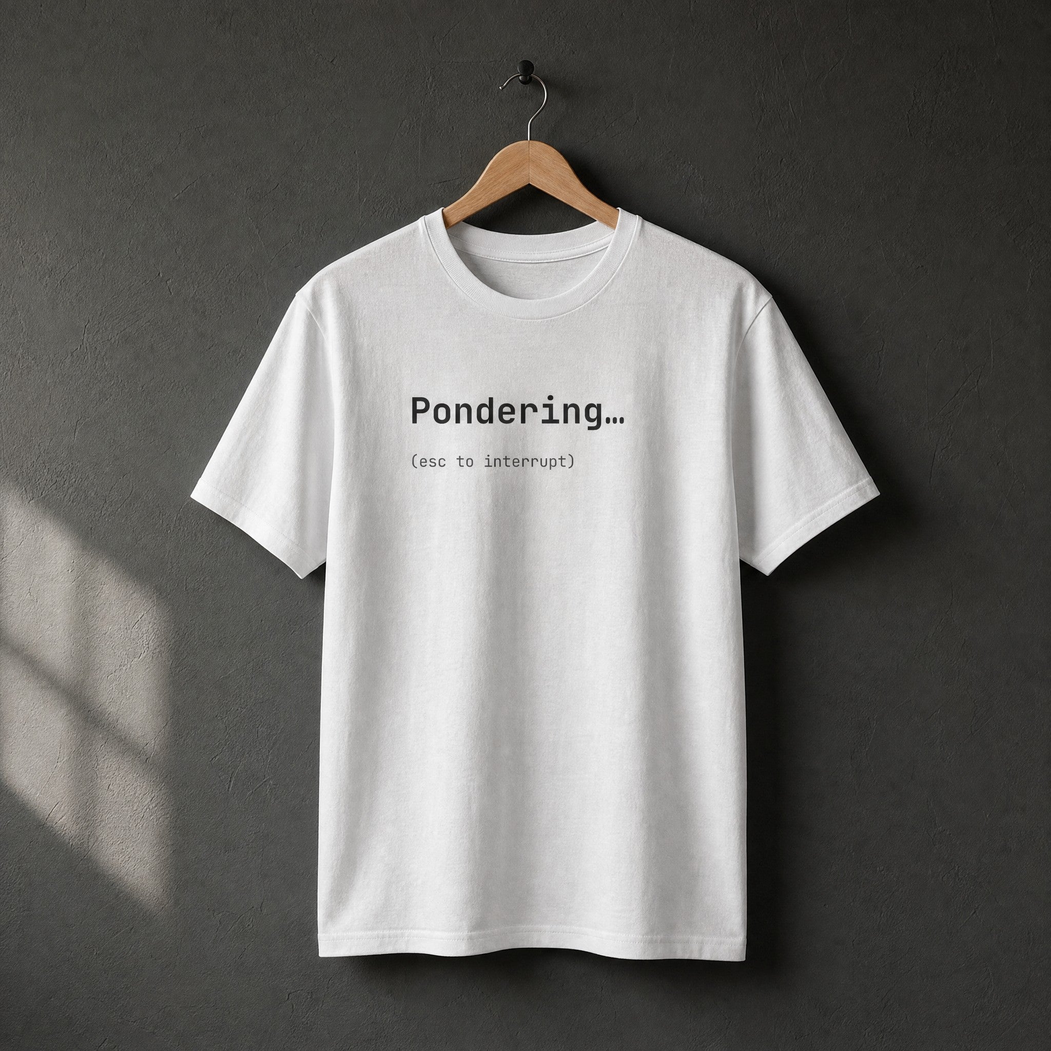White Pondering esc to interrupt t-shirt on a wooden hanger